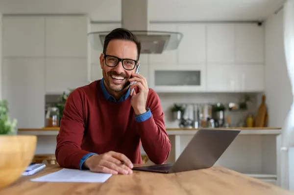 Homme souriant avec téléphone et ordinateur portable.